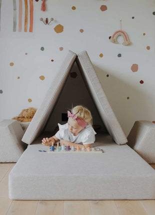 Kind ligt in een tentvormige speelconstructie van de beige Monboxy Montessori speelbank – stimuleert fantasierijk en zelfstandig spel.