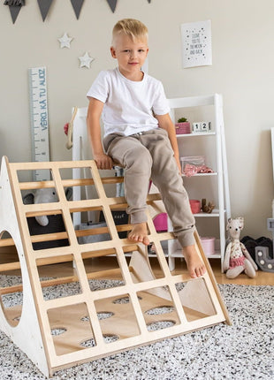 Kind zit bovenop de Berkenhouten Montessori Klimdriehoek in een ingerichte speelkamer.