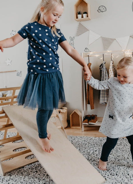 Twee kinderen spelen op en naast de Berkenhouten Montessori Klimdriehoek met Helling.