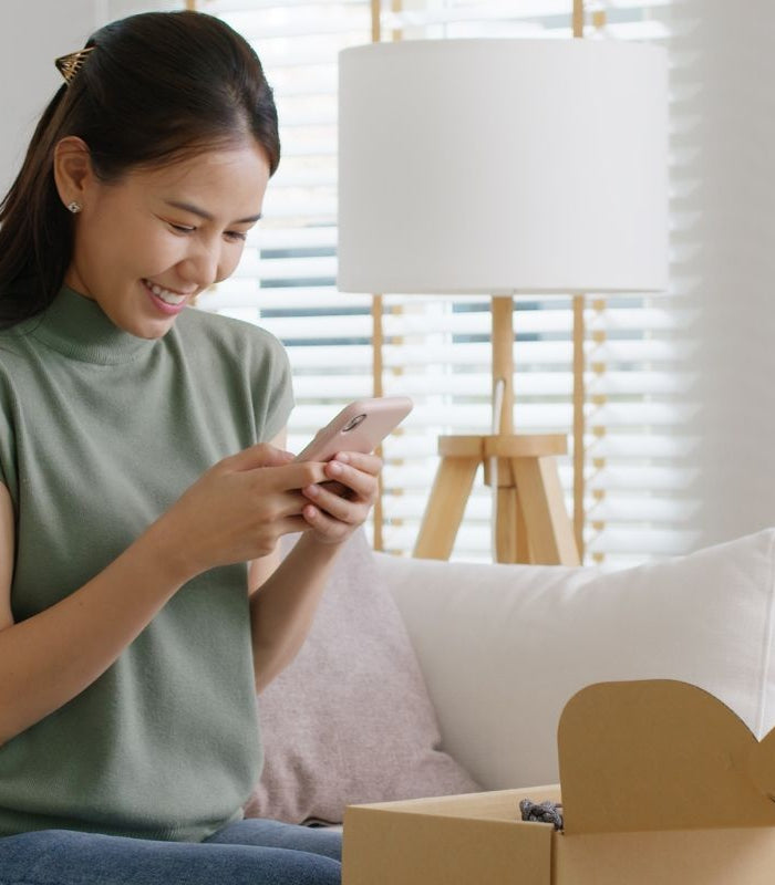 Vrouw zit op bank met open pakket, glimlacht terwijl ze contact opneemt via haar telefoon met de klantenservice van Cunavo.