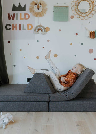 Kind ontspant in ligstoelconfiguratie van de donkerbruine Montessori speelbank – multifunctioneel voor relaxmomenten.