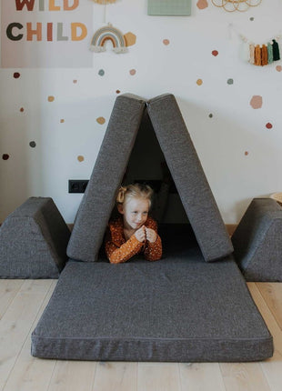 Kind ligt ontspannen in een tentvormige opstelling van de donkerbruine Monboxy Montessori speelbank – bevordert geborgenheid en rust.
