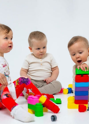 Drie peuters spelen zittend op witte achtergrond met Gerardo’s Toys Biologische Zachte Bouwblokken.