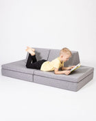 Kind ligt te lezen op de bankopstelling  van de Monboxy Montessori speelbank – stimuleert zelfstandige ontspanning.