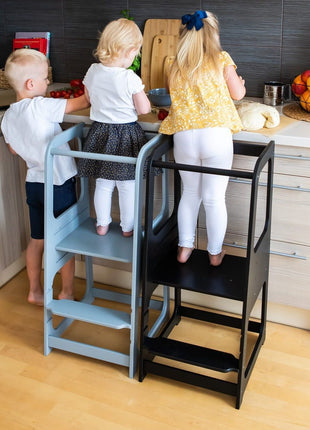 Grijze en zwarte Keukenhulp Toren met twee kinderen erop en derde kind aan aanrecht.