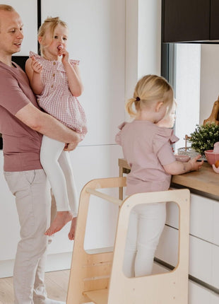 Keukenhulp Toren met kind dat aanrecht onderzoekt, tweede kind op arm van volwassene.