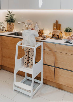 Witte Keukenhulp Toren met kind dat bij aanrecht koekjesvormpjes vasthoudt.