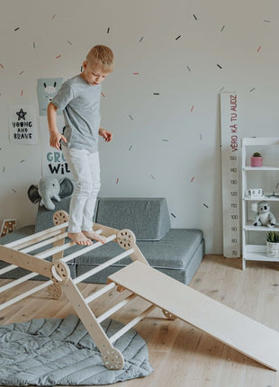 Jongen balanceert op de top van de Montessori klimdriehoek – ontwikkelt zelfvertrouwen, balans en grove motoriek op een veilige manier.