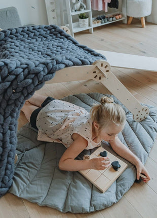 Kind speelt in een zelfgemaakte speeltent met de Montessori klimdriehoek – creatief gebruik van de structuur bevordert fantasierijk en sensorisch spel.