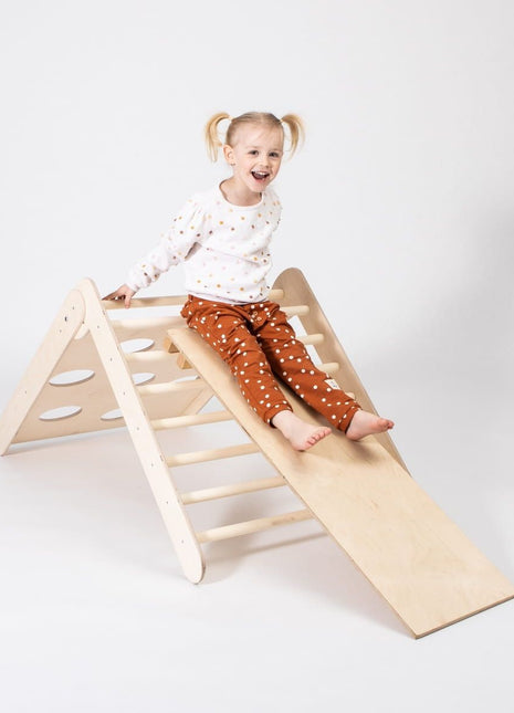 Kind glijdt lachend van houten helling van Montessori klimdriehoek – stimuleert balans en zelfvertrouwen.