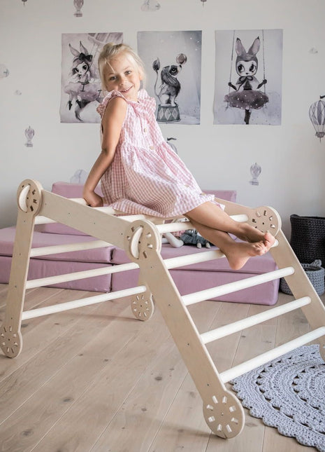 Meisje zit boven op een houten klimdriehoek in een speelhoek – perfect voor fantasierijk Montessori spel.