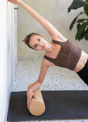 Volwassene gebruikt Leg&Go kurkroller liggend op yogamat tegen muur