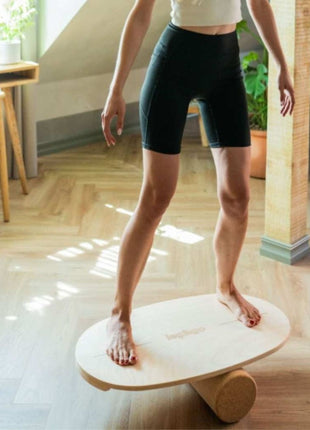 Volwassene balanceert staand op rond Leg&Go balansbord met kurkroller in woonkamer