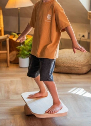 Kind oefent balans op het Leg&Go balansbord met oefenrol op een houten vloer.