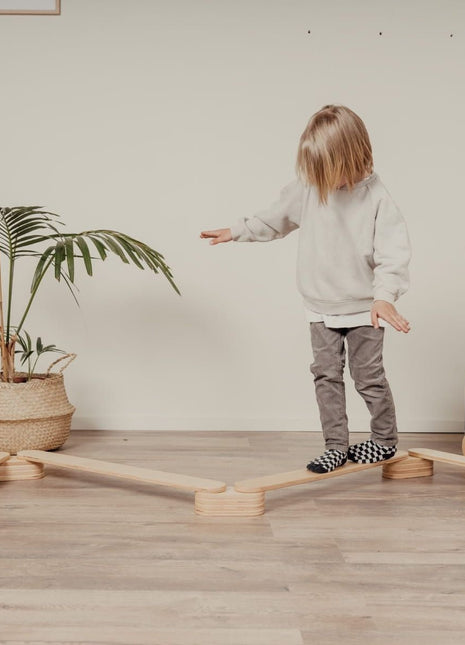 Kind balanceren op de Leg&Go evenwichtsbalkenset van 4 naast een plant in een binnenruimte.