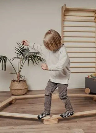 Kind balanceerd op de Leg&Go evenwichtsbalkenset van 6 in zeshoekige opstelling naast een klimrek.