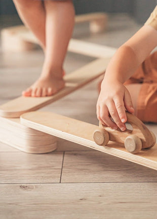 Kind speelt met houten auto op een balk van de Leg&Go evenwichtsbalkenset van 4.