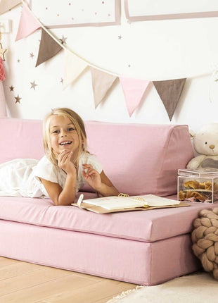 Lachend meisje op roze Monboxy speelbank in sfeervolle kinderkamer met vlaggetjes en knuffels.