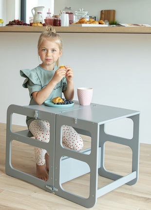 Meisje zit aan grijze Montessori 2-in-1 Keukentoren in tafelstand met ontbijt.