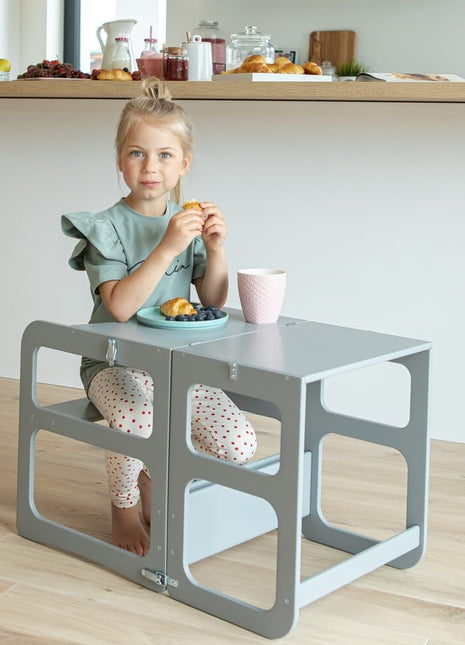 Meisje zit aan grijze Montessori 2-in-1 Keukentoren in tafelstand met ontbijt.