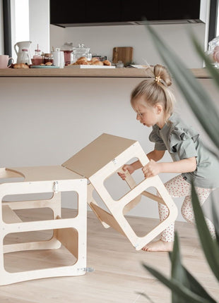 Meisje klapt onderdeel uit van naturel Montessori 2-in-1 Keukentoren in keuken.