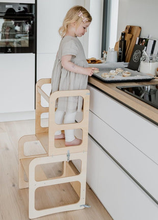 Meisje staat op de naturel Montessori 2-in-1 Keukentoren bij keukenblad.