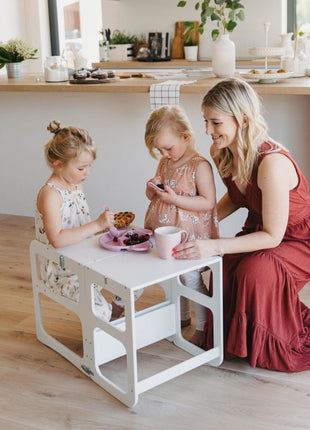 Twee kinderen en een volwassene aan witte Montessori 2-in-1 Keukentoren in tafelstand.
