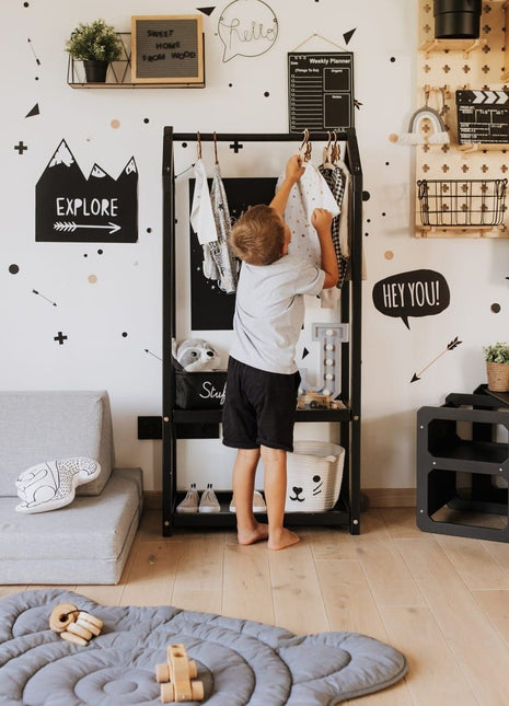 Jongen hangt kleding op Montessori Huisvormig Kledingrek in zwarte variant in kinderkamer.