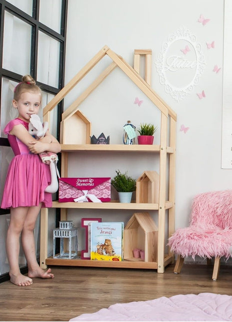 Montessori Huisvormige Plankenkast met meisje in roze jurk en knuffel in speelhoek.
