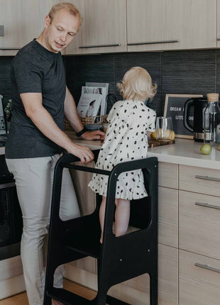 Montessori Keukenhulp met Schoolbord in zwart waarop kind staat naast vader in keuken.