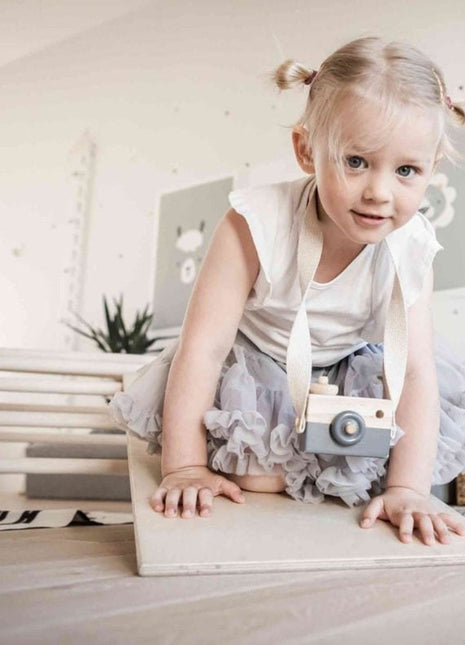 Kind kruipt op de helling van de Montessori Klimboog richting de camera met speelgoedcamera om de nek.