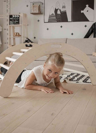 Kind ligt op de grond en kijkt lachend onder de Montessori Klimboog door in een speelkamer.