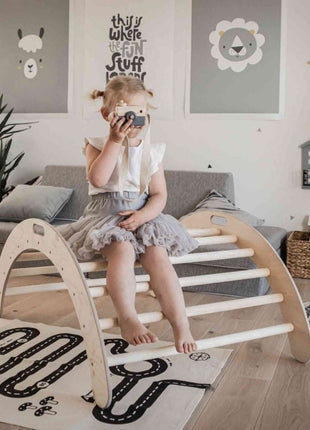 Kind zit op de Montessori Klimboog met een houten speelgoedcamera in een speelkamer.