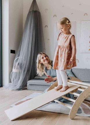 Kind loopt op de helling van de Montessori Klimboog met Helling onder aanmoediging van volwassene.