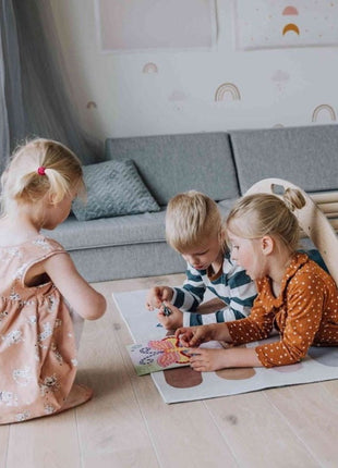 Drie kinderen spelen op de vloer en onder de Montessori Klimboog met Helling in een speelkamer.