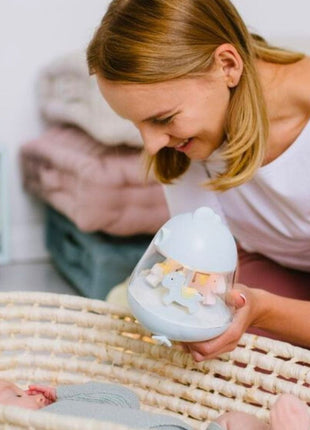 Montessori nachtlampje blauw met draaiende paarden, moeder toont lampje aan baby in een wieg.