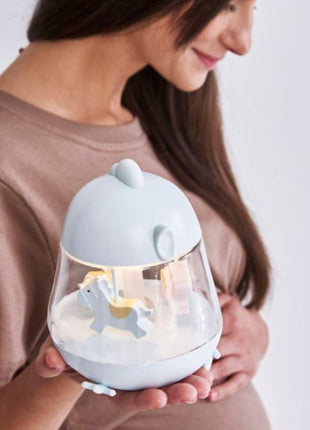 Montessori nachtlampje blauw brandend met draaiende paarden, vastgehouden door zwangere vrouw.