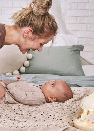 Montessori nachtlampje geel op bed, moeder lacht naar baby, sfeervol gebruiksmoment.