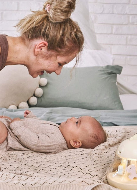 Montessori nachtlampje geel op bed, moeder lacht naar baby, sfeervol gebruiksmoment.