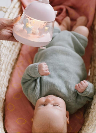 Montessori nachtlampje roze met draaiende paarden, gebruikt naast baby in een wieg.