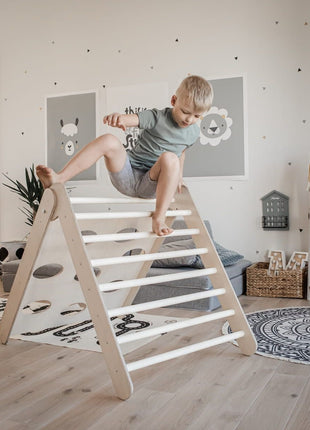 Kind klimt tot bovenop de houten klimdriehoek – uitgedaagd om grenzen te verkennen in veilige speelruimte.