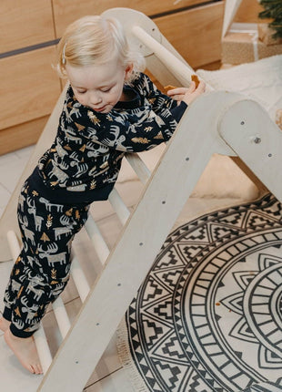 Peuter klimt op houten klimdriehoek in huiselijke speelhoek – versterkt motoriek en zelfvertrouwen.