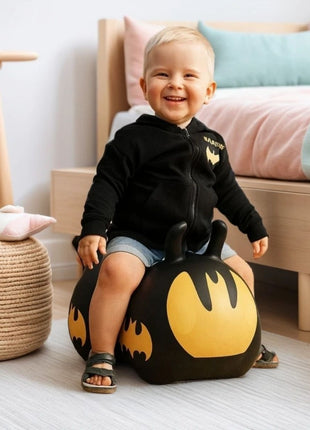 Peuter speelt op zwarte My First Jumpy Batmobiel springauto bij kinderbed met roze dekbed.