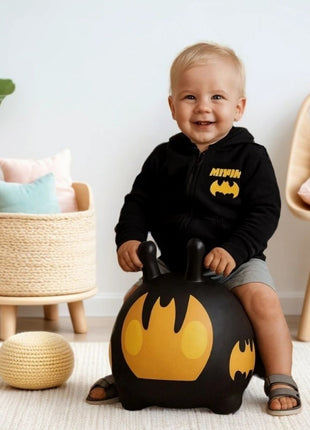 Peuter zit op zwarte My First Jumpy Batmobiel springauto in speelkamer met mand en stoel.
