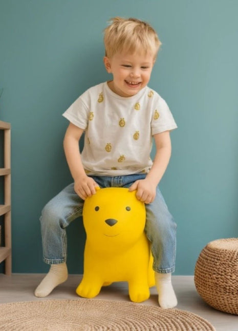 Kind zit op My First Jumpy geel springbeer bij blauwe muur en rotan poef.