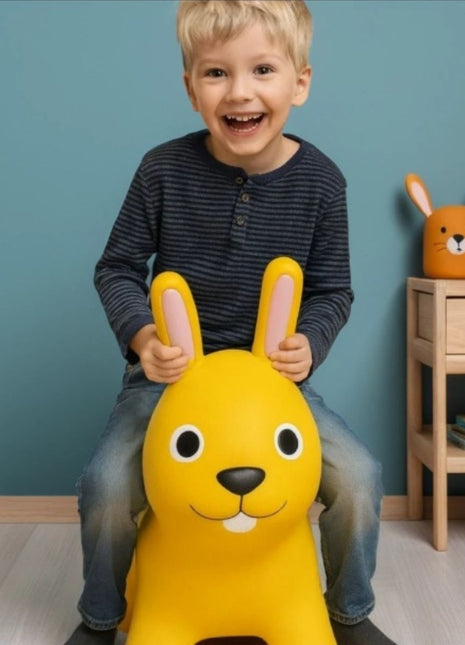 Kind zit op My First Jumpy geel springkonijn bij houten nachtkastje.