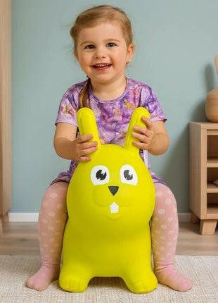 Kind zit op My First Jumpy groen springkonijn bij houten kast en decoratievaas.