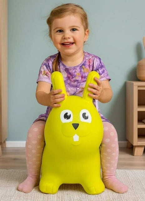 Kind zit op My First Jumpy groen springkonijn bij houten kast en decoratievaas.