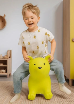 Kind zit op My First Jumpy groene springbeer bij gele kast in kinderkamer.