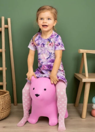 Kind zit op My First Jumpy roze springbeer bij groene muur en houten meubel.